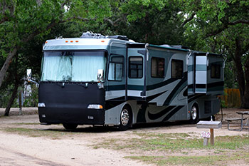 a recreational vehicle ( R V ) parked near trees at a camp site